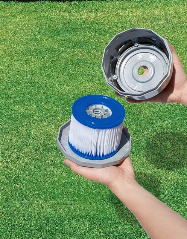 Hands holding and opening the Lay-Z-Spa hot tub filter cartridge with blue rim on a grassy background.